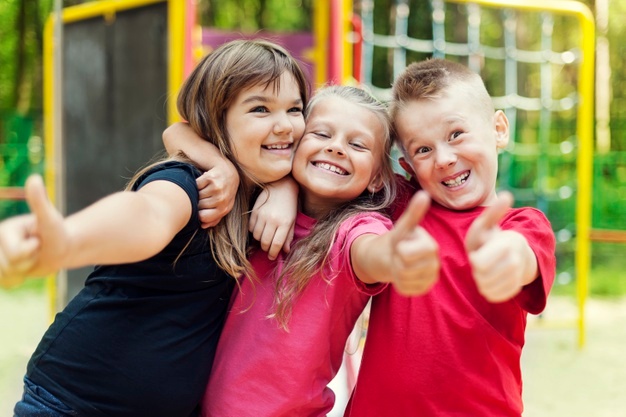 trois enfants souriants posant les pouces levés dans un cadre très coloré