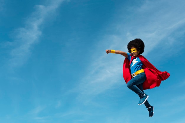 enfant habillé en superhéros volant le poing en avant dans un ciel bleu